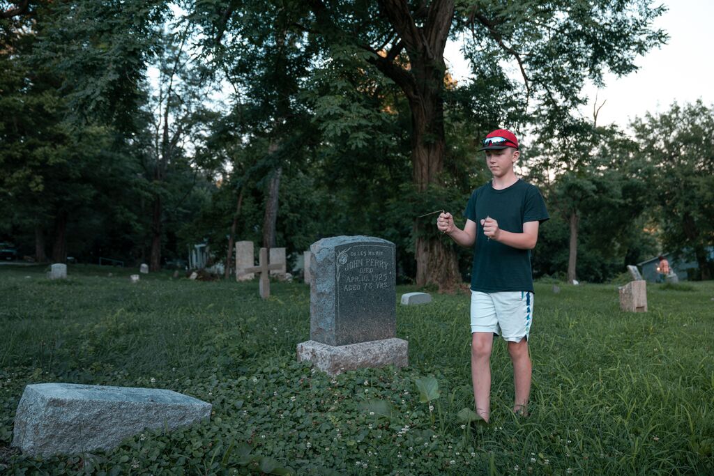 A person carries divining rod through an old cemetery with stone grave markers.