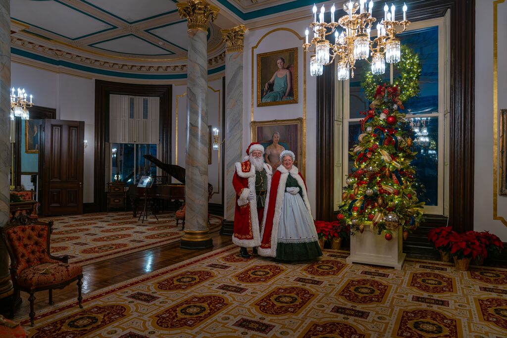 Actors portraying Santa and Mrs. Claus stand beside a multi-colored decorated Christmas tree in the Missouri Governor's Mansion during its annual candlelit tours. 