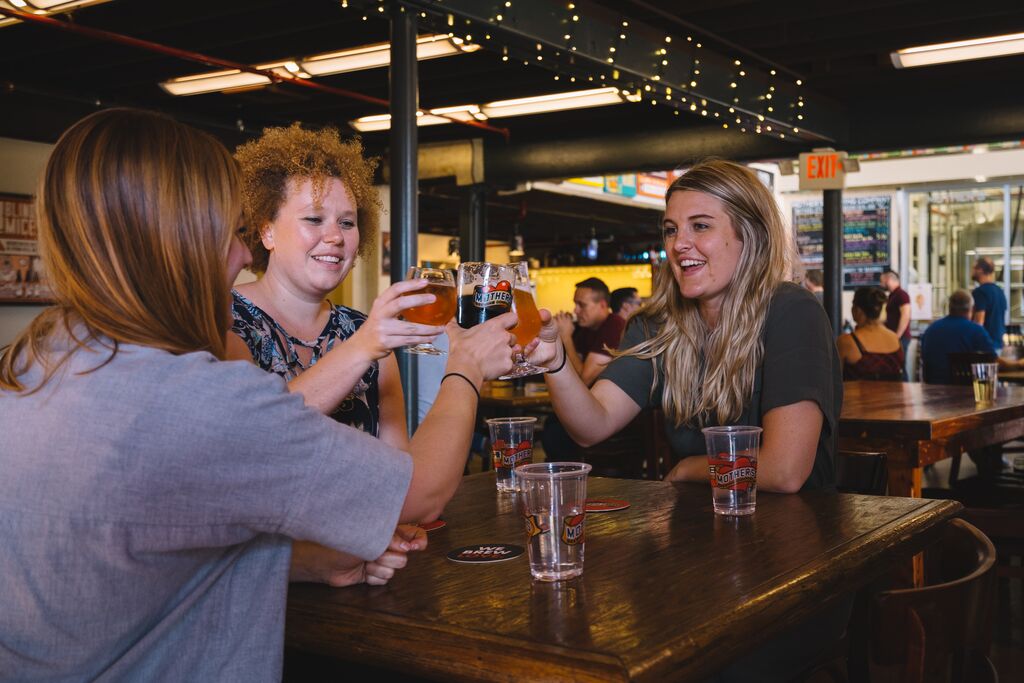 Three people raise their glasses at a table at a brewery