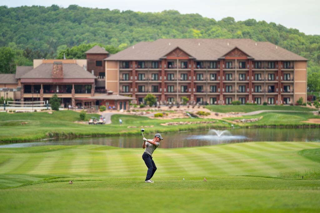 Person teas off at golf course with rustic resort in the background.