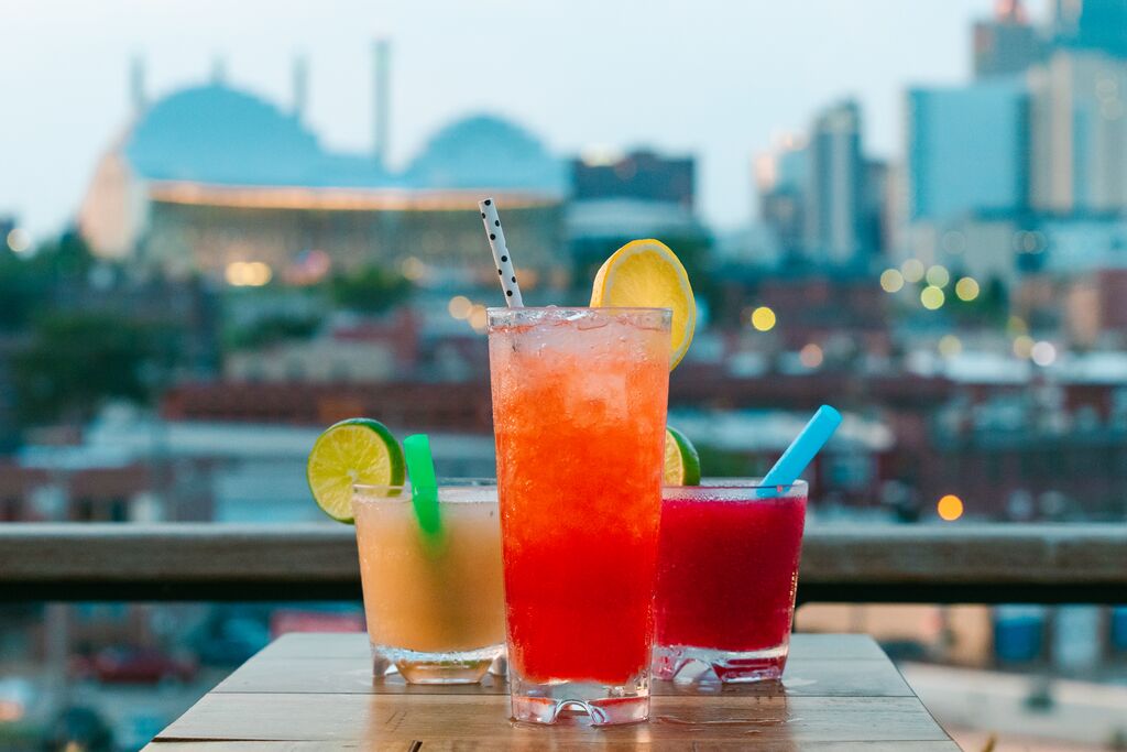 Craft cocktails sit on a table with the Kansas City skyline in the background at Percheron Rooftop Bar.